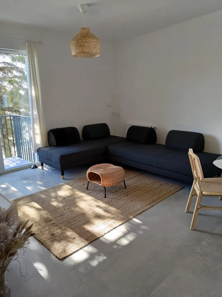 Narożna granatowa sofa na jutowym dywanie w pełnym porannego światła salonie